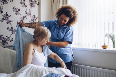 Caregiver helping a senior woman to get dressed in her bedroom